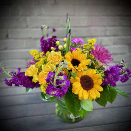 Bouquet of yellow sunflowers and purple flowers in a glass vase