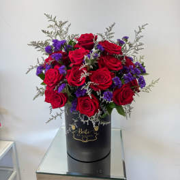 Red roses and purple filler flowers in a black hatbox