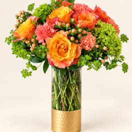 Orange and coral roses with pink carnations in a glass vase