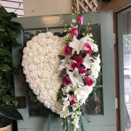 Heart-shaped white floral wreath with pink roses and lilies on an easel