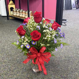 Red roses and purple daisies in a glass vase with a red ribbon