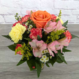 Mixed bouquet with an orange rose, pink lilies, and yellow carnations in a vase