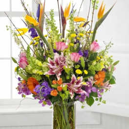 Tall mixed bouquet in a clear glass vase with pink, purple, orange, and yellow flowers