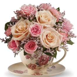 Pink and cream roses arranged in a floral teacup with saucer
