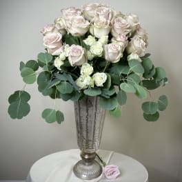Tall silver urn with blush and ivory roses and greenery on a draped round table