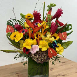 Tropical bouquet with yellow sunflowers and red-orange blooms in a green vase