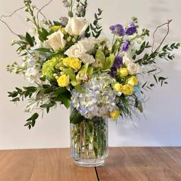 Mixed bouquet of white, yellow, purple, and blue flowers in a glass vase