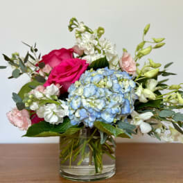 Mixed bouquet with pink roses, blue hydrangea, and white flowers in a glass vase