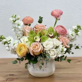 Mixed bouquet of pastel roses, ranunculus, and white blooms in a ceramic vase