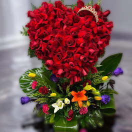 Tall arrangement with a heart of red roses above mixed colorful blooms and a gold tiara accent.