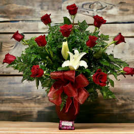 Tall arrangement of red roses and white lilies in a red vase with red bow and chocolates