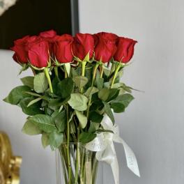 Tall bouquet of red roses in a clear glass vase with a white ribbon