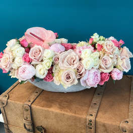 Low floral arrangement of pale pink and white roses with anthurium in a gray container