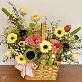 Mixed flower arrangement in a woven basket with a pink ribbon