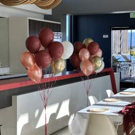 Clusters of burgundy, blush, gold, and white balloons in a decorated room