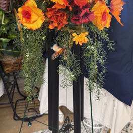 Orange and red floral arrangement with trailing greenery and a butterfly accent