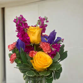 Colorful bouquet of yellow roses, purple irises, and pink flowers in a glass vase