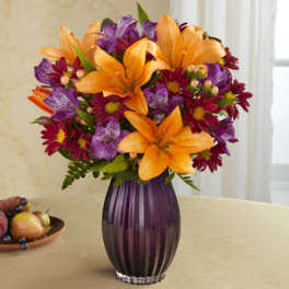 Orange lilies and purple daisies in a purple glass vase
