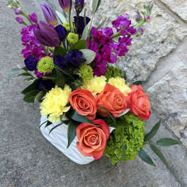 Colorful bouquet with roses, tulips, and purple blooms in a white vase
