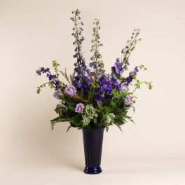 Tall purple floral arrangement in a blue vase