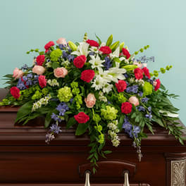 Large casket spray of red carnations, white lilies, pink roses, green blooms and blue delphinium