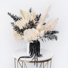 White floral arrangement with black and beige dried accents in a black vase