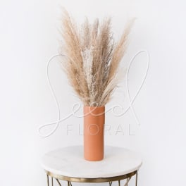 Tall dried pampas grass in a terracotta vase on a round table