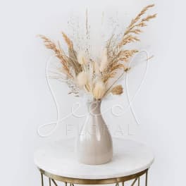 Dried grass arrangement in a beige vase on a round table