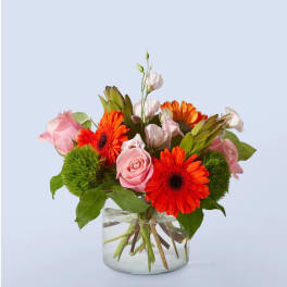 Pink roses and orange gerbera daisies in a clear glass vase
