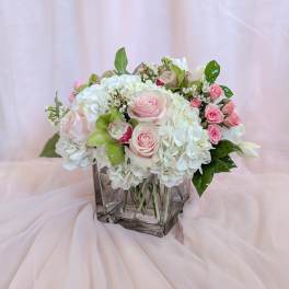 Pink and white floral arrangement in a square glass vase
