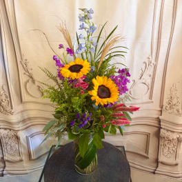 Tall mixed bouquet with sunflowers, purple blooms, and a glass vase