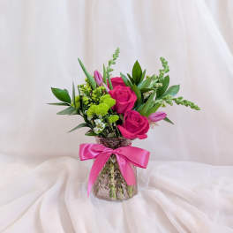 Pink roses and green flowers in a glass vase with a pink ribbon
