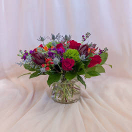 Mixed bouquet of red roses and purple flowers in a clear glass vase