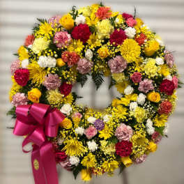 Bright standing wreath of yellow, pink, white, and red flowers with a hot pink ribbon bow