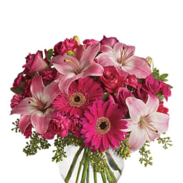 Pink lilies, gerbera daisies, roses, and carnations in a clear glass vase