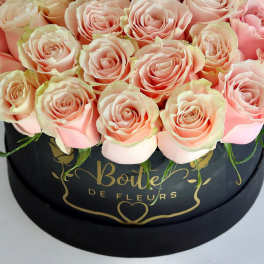 Pink roses arranged in a black round box with gold lettering