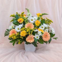 Mixed bouquet of peach gerbera daisies, yellow roses, and white daisies in a white vase