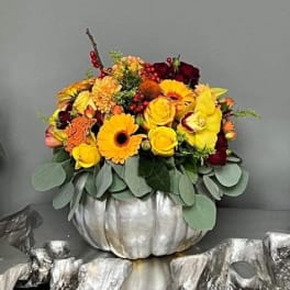 Yellow and burgundy floral arrangement in a silver pumpkin container