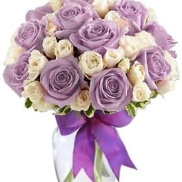 Lavender and white rose bouquet in a clear glass vase with a purple ribbon