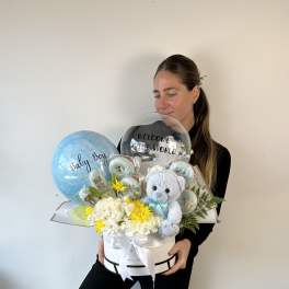 Baby gift arrangement with balloons, flowers, and a teddy bear in a white box