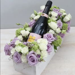 Lavender and white roses arranged around a champagne bottle in a white box