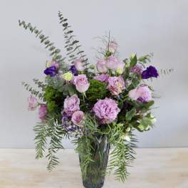 Pink and purple bouquet in a glass vase with trailing greenery