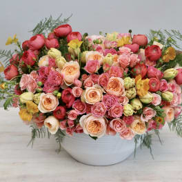 Large bouquet of pink, peach, and red roses in a white bowl vase