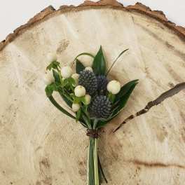 Small boutonniere with white berries and blue thistle on a wood slice