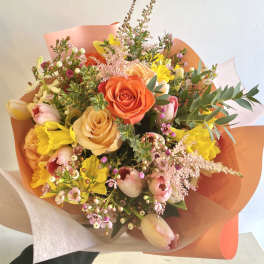 Bouquet of orange, peach, pink, and yellow flowers wrapped in coral paper