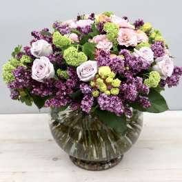Mixed bouquet of pink and lavender flowers in a round glass vase