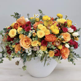 Mixed bouquet of yellow, orange, and red flowers in a white vase
