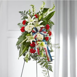 Standing floral spray with white lilies, red carnations, and ribbon on an easel