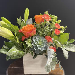 Orange roses and lilies in a square wooden container with succulents