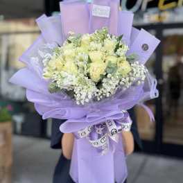 Lavender-wrapped bouquet of pale yellow and white flowers